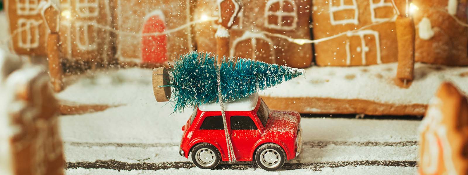 rotes Spielzeugauto mit Weihnachtsbaum fährt in einer Lebkuchenstadt